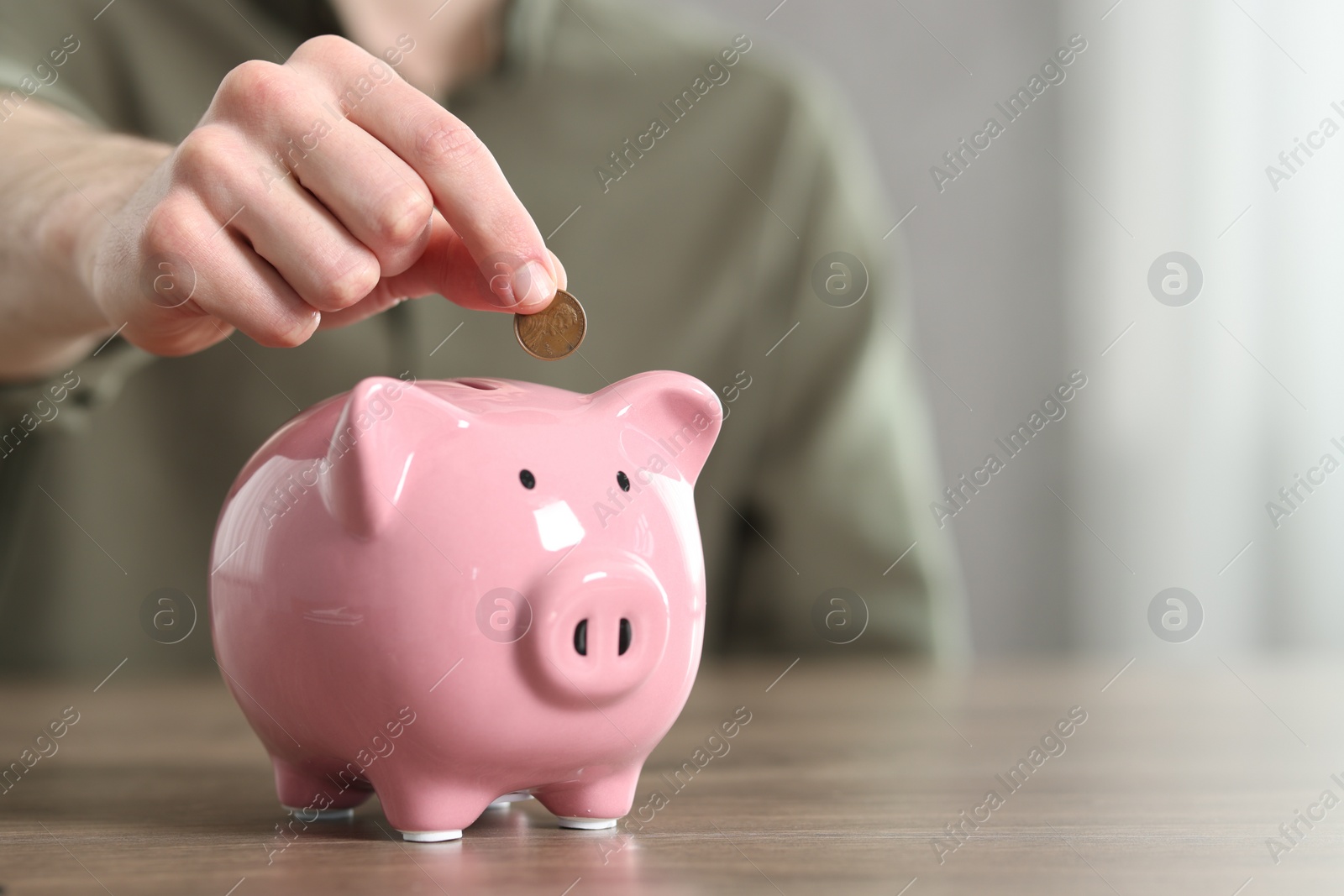 Photo of Financial savings. Man putting coin into piggy bank at wooden table, closeup. Space for text