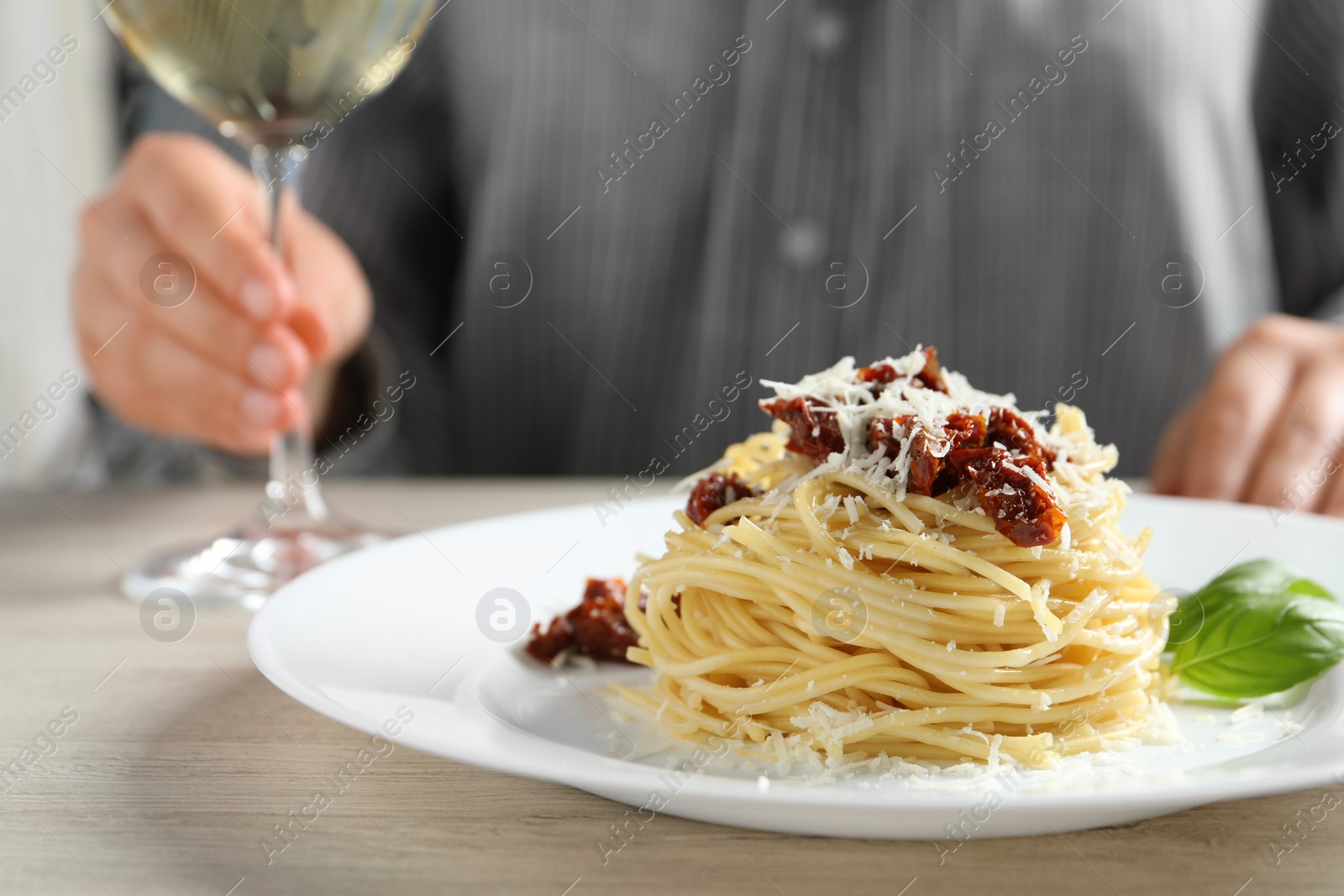 Photo of Woman enjoying tasty spaghetti with sun-dried tomatoes and parmesan cheese and wine at wooden table in restaurant, closeup. Exquisite presentation of pasta dish