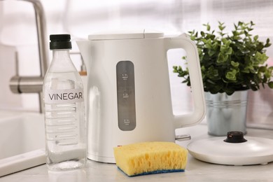 Photo of Cleaning electric kettle. Bottle of vinegar and sponge on countertop in kitchen
