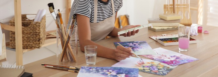 Image of Young woman drawing flowers with watercolors at table indoors, closeup. Banner design
