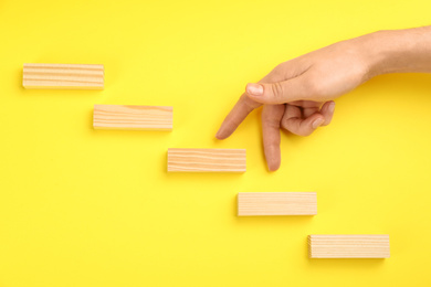 Photo of Closeup view of woman imitating stepping up on wooden stairs with her fingers, yellow background. Career promotion concept