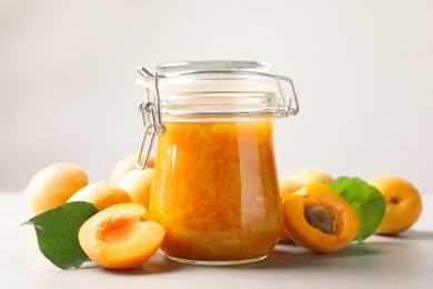 Photo of Jar of apricot jam and fresh fruits on light table