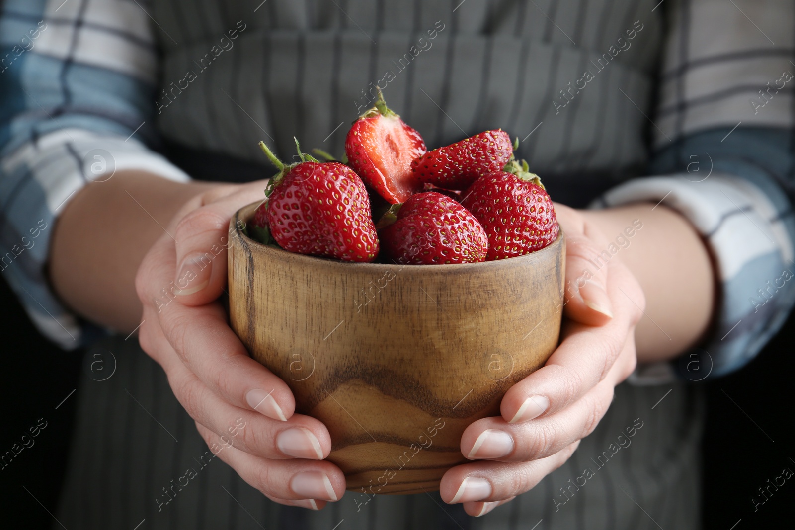 Photo of Woman holding bowl with tasty fresh strawberries on black background, closeup