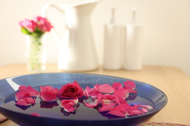 Photo of Pink roses and petals in bowl with water on table, closeup. Space for text