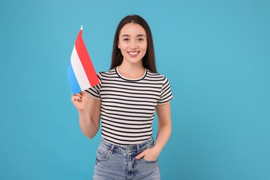 Photo of Young woman holding flag of Netherlands on light blue background
