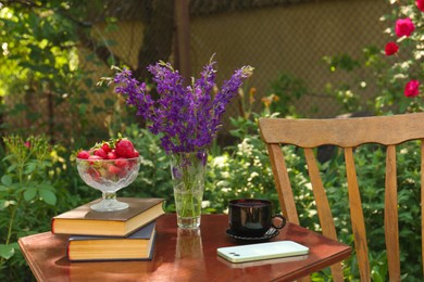Beautiful bouquet of wildflowers, smartphone, strawberries and books on table in garden