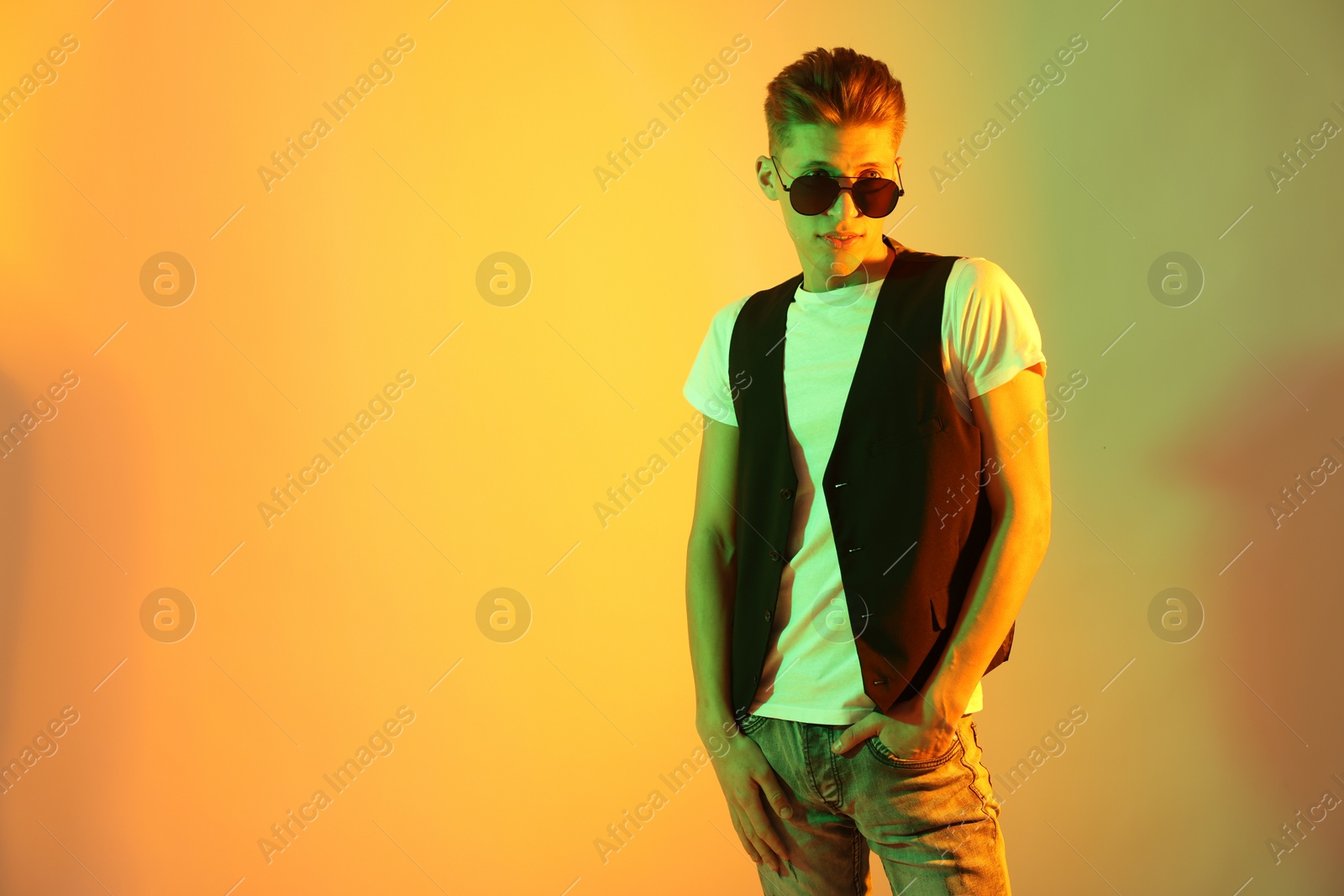 Photo of Stylish young man in sunglasses on color background in neon lights. Space for text