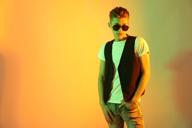 Photo of Stylish young man in sunglasses on color background in neon lights. Space for text