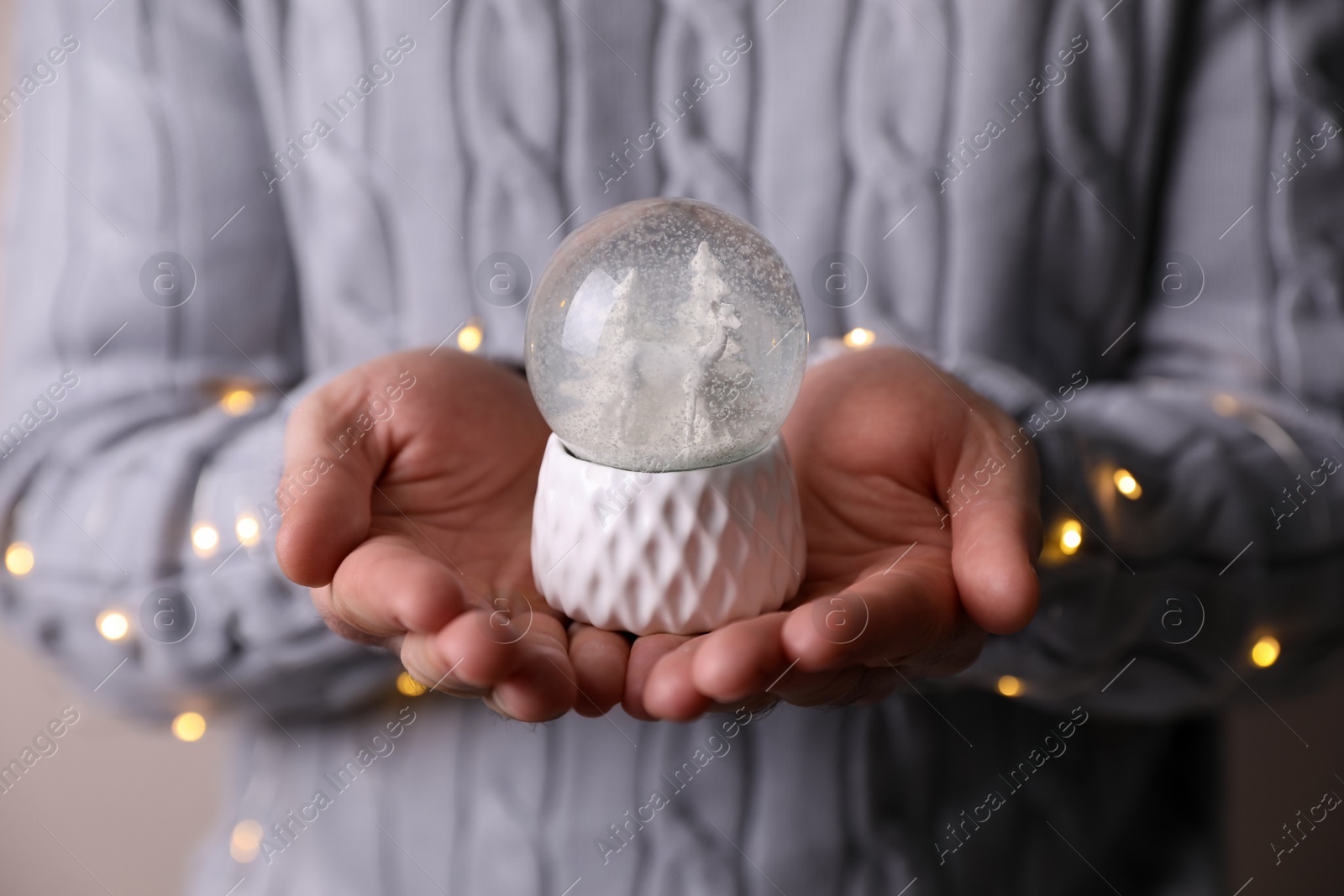 Photo of Man in warm sweater holding snow globe and fairy lights, closeup
