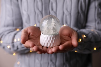 Photo of Man in warm sweater holding snow globe and fairy lights, closeup