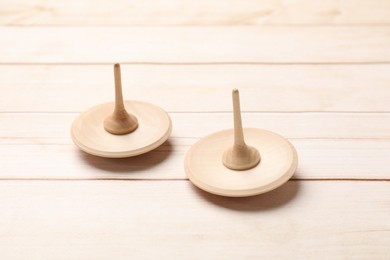 Photo of Two spinning tops on light wooden table, closeup