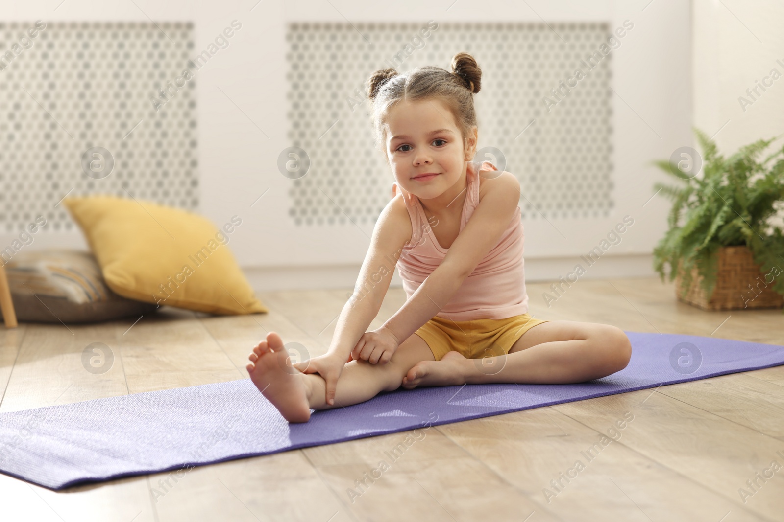 Photo of Little cute girl stretching herself on mat at home