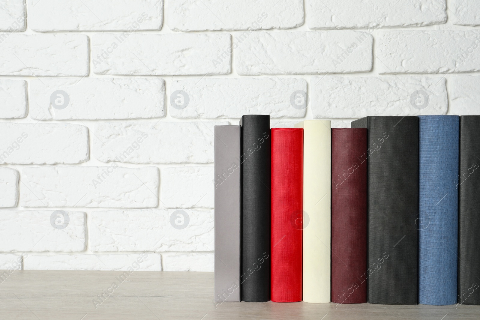 Photo of Many different hardcover books on grey table near white brick wall, space for text