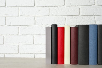 Photo of Many different hardcover books on grey table near white brick wall, space for text