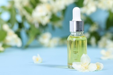 Photo of Essential oil in bottle and beautiful jasmine flowers on light blue background, closeup. Space for text