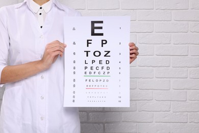 Photo of Ophthalmologist with vision test chart near white brick wall, closeup