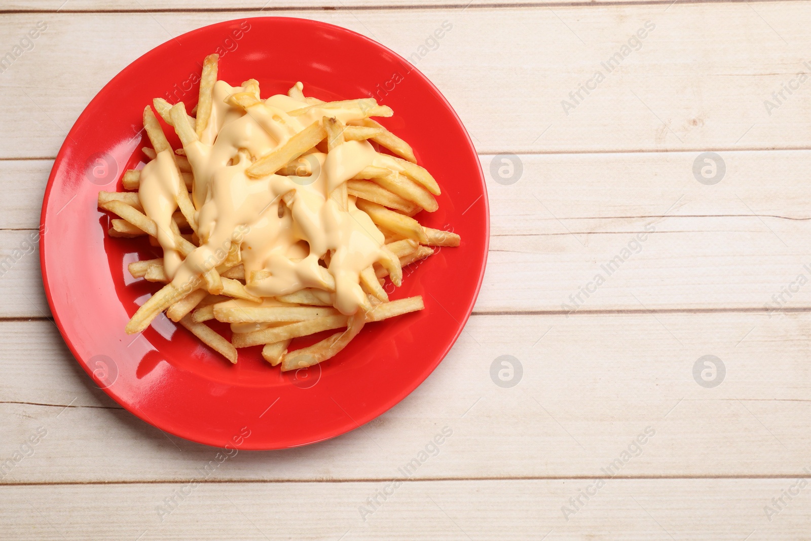 Photo of Delicious french fries with cheese sauce on wooden table, top view. Space for text