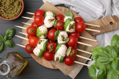 Caprese skewers with tomatoes, mozzarella balls and basil on grey wooden table, flat lay