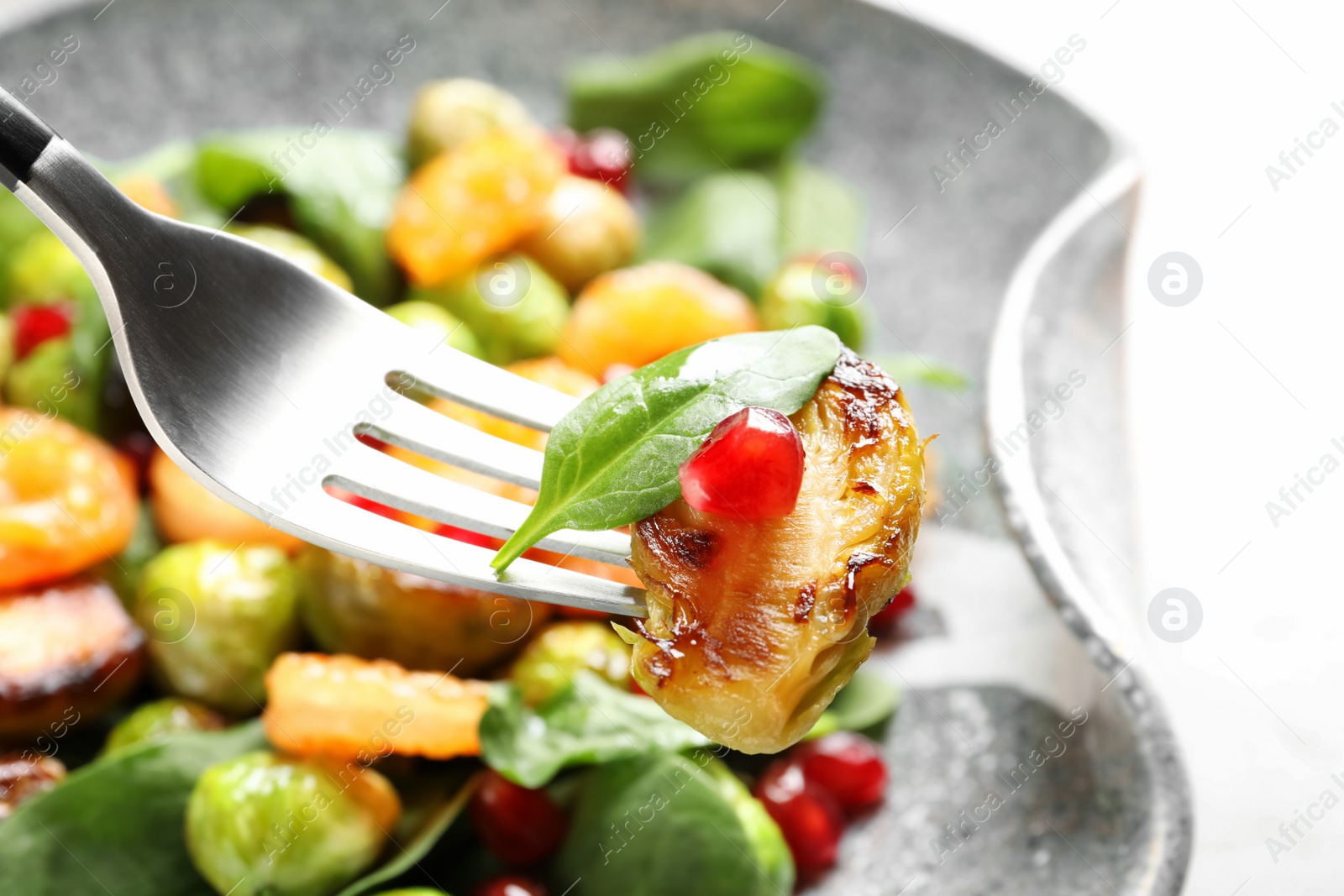 Photo of Fork with warm Brussels sprouts salad over table, closeup