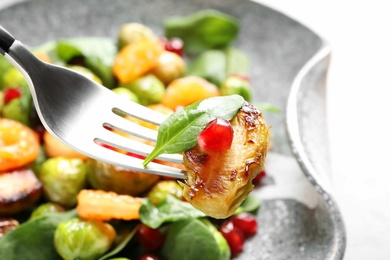 Photo of Fork with warm Brussels sprouts salad over table, closeup