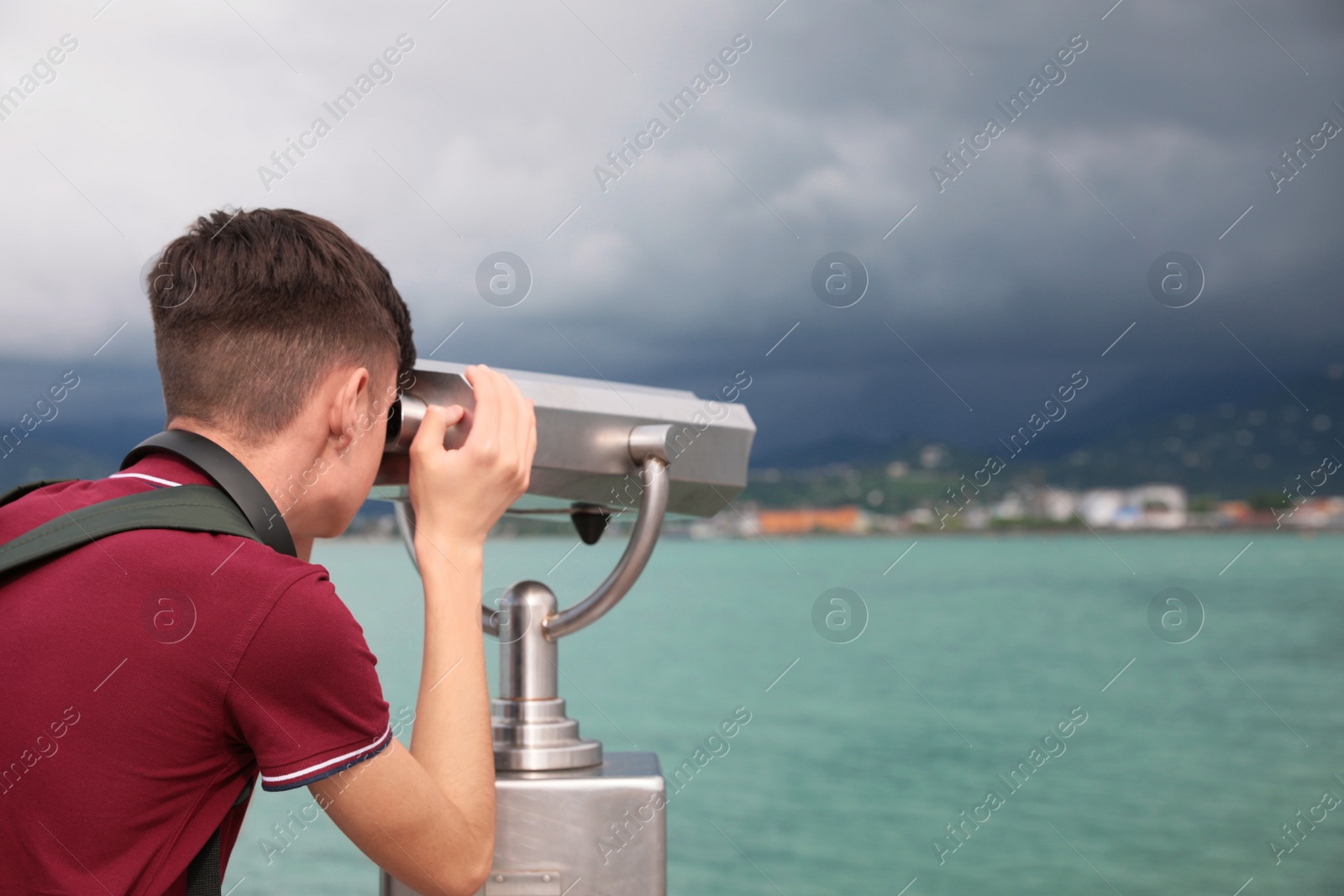 Photo of Teenage boy looking through mounted binoculars at mountains. Space for text