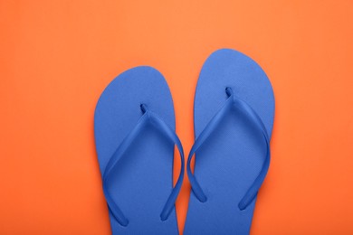 Stylish blue flip flops on orange background, top view