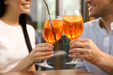 Photo of Couple clinking glasses of Aperol spritz cocktails outdoors, closeup