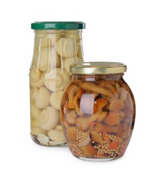 Jars with marinated mushrooms on white background