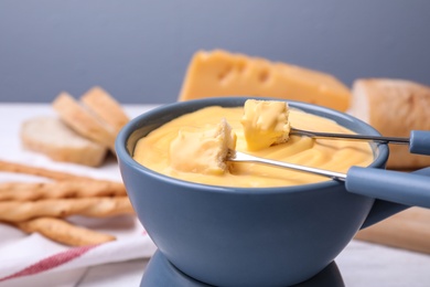 Pot with delicious cheese fondue and bread pieces on table