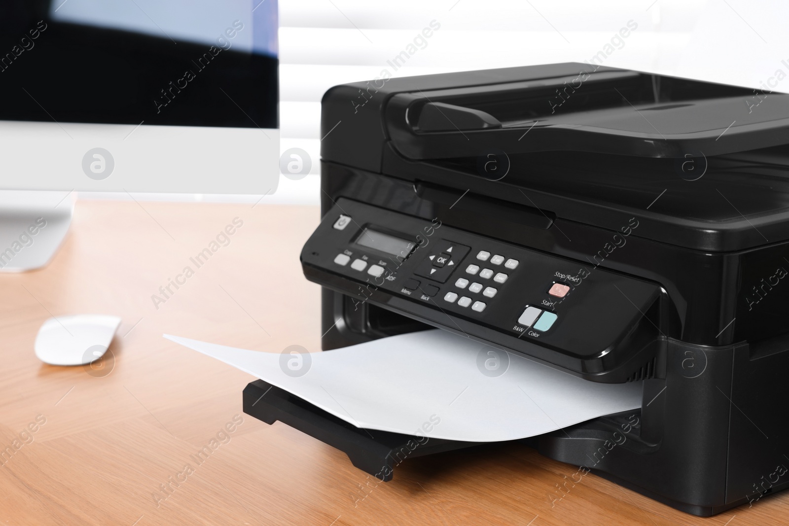 Photo of Modern printer with paper near computer on wooden table in office