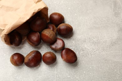Photo of Paper bag with roasted edible sweet chestnuts on light grey table, top view. Space for text