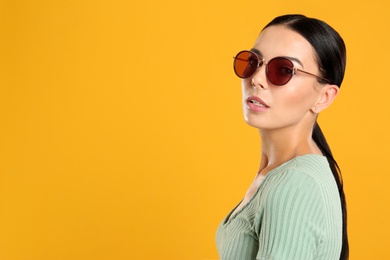 Photo of Beautiful woman wearing sunglasses on yellow background. Space for text