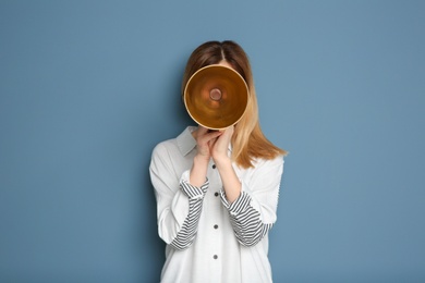 Young woman shouting into megaphone on color background