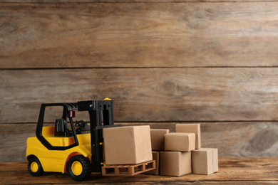 Forklift model and carton boxes on wooden background, space for text. Courier service