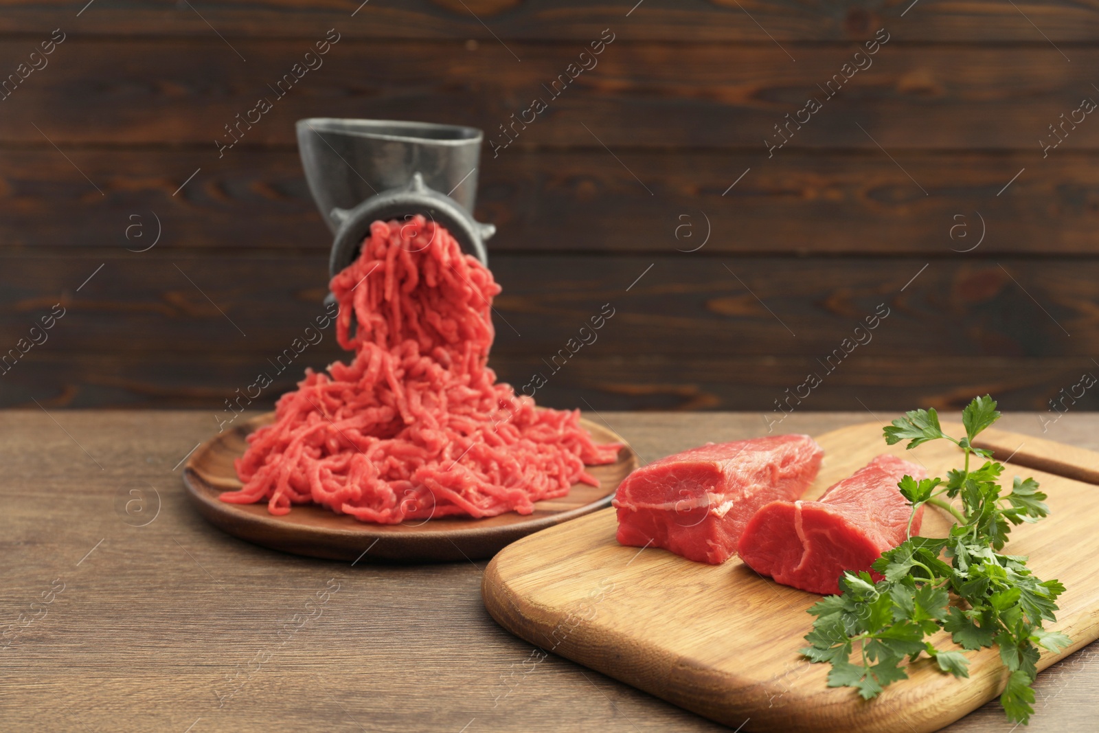 Photo of Manual meat grinder with beef and parsley on wooden table, space for text