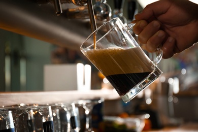 Bartender pouring beer into glass in pub, closeup