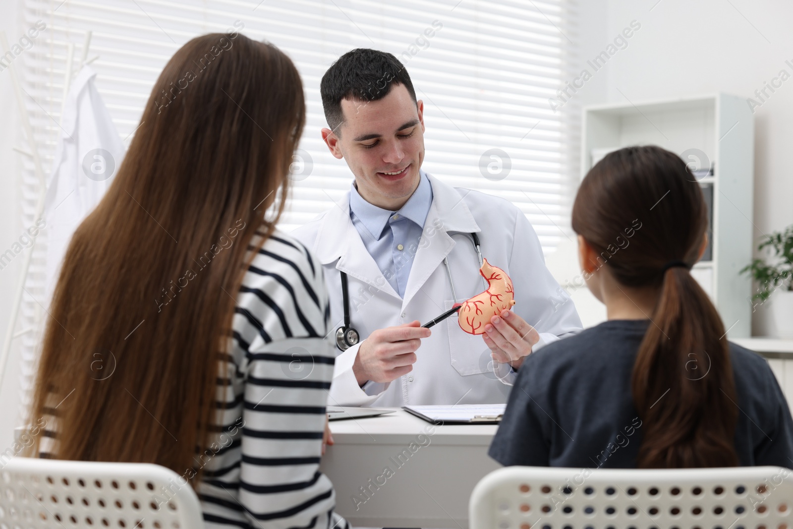 Photo of Gastroenterologist with model of stomach consulting woman and her daughter in clinic