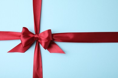 Red satin ribbon with bow on light blue background, top view