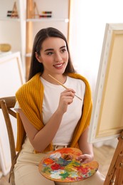 Beautiful young woman drawing on easel at home