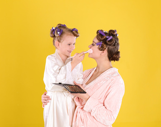 Happy daughter applying powder onto mother's face on yellow background
