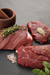 Photo of Pieces of raw beef meat, mortar with pestle and spices on black table