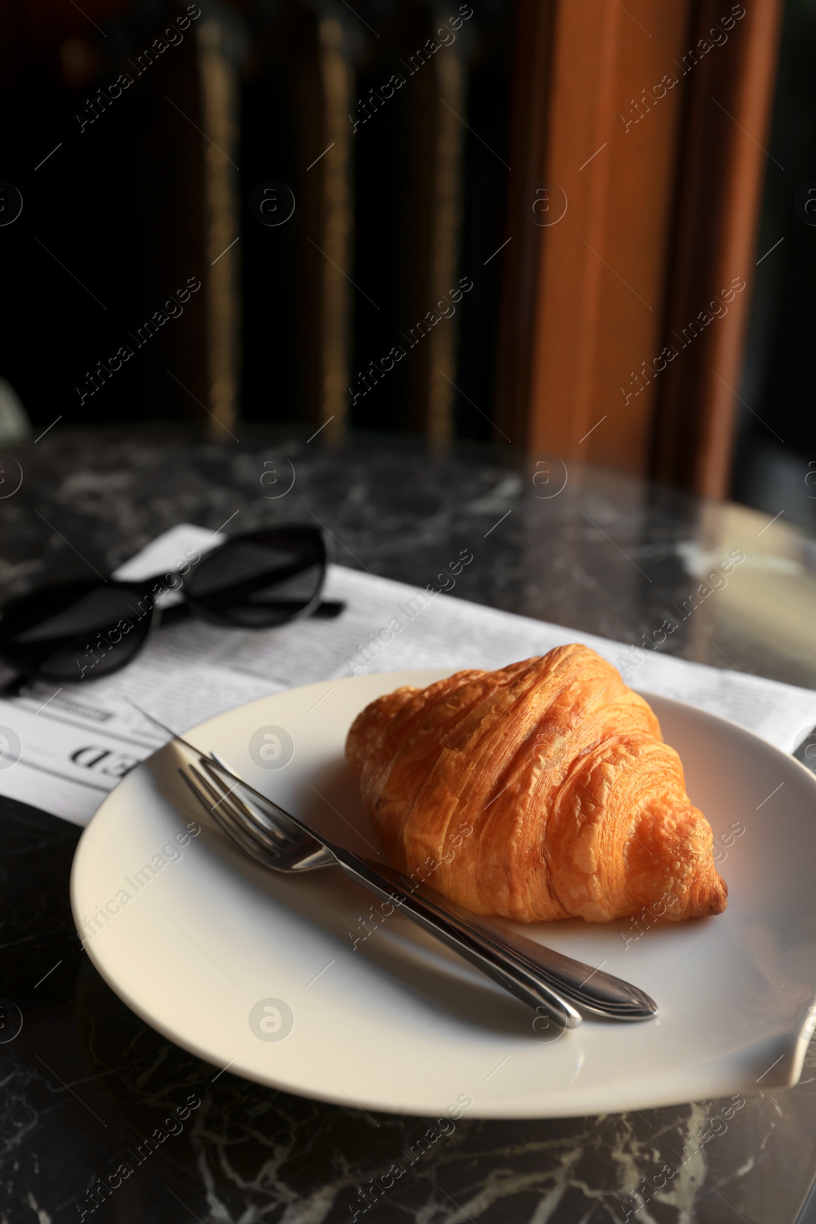 Photo of Tasty croissant, newspaper and sunglasses on black table