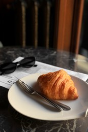 Tasty croissant, newspaper and sunglasses on black table