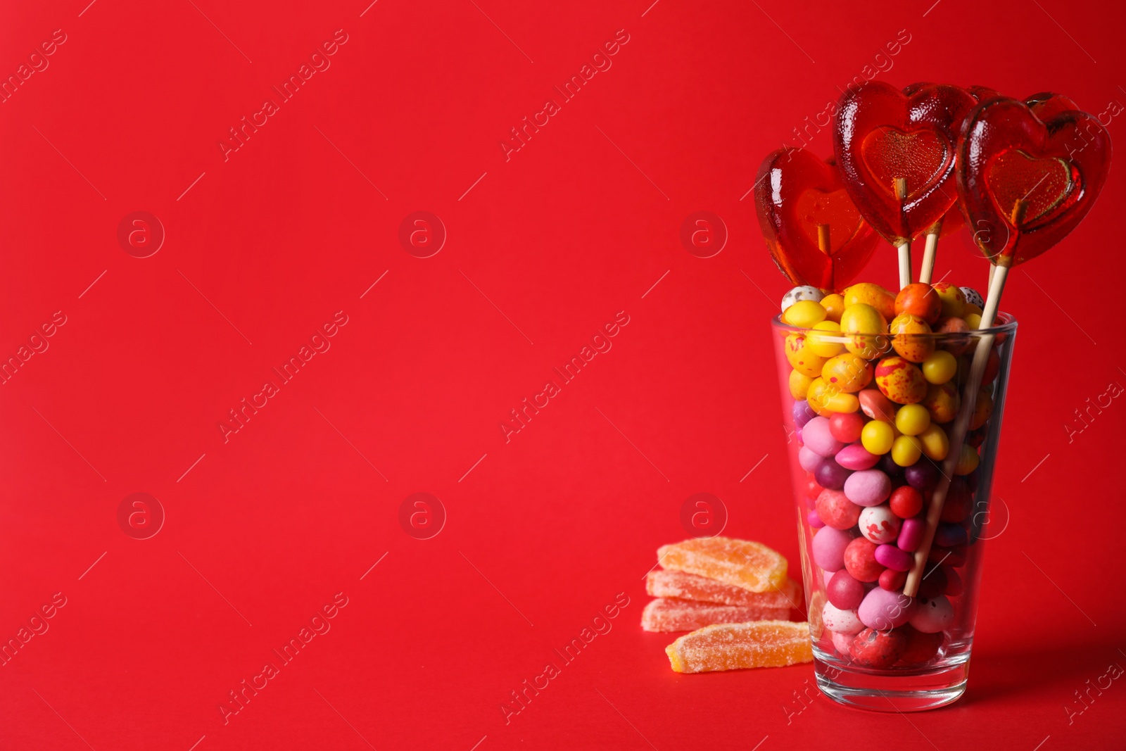 Photo of Glass with different candies on red background, space for text