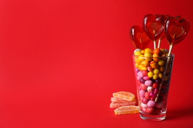Photo of Glass with different candies on red background, space for text