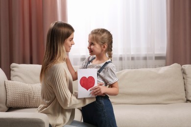 Photo of Little daughter congratulating mom with greeting card at home. Happy Mother's Day