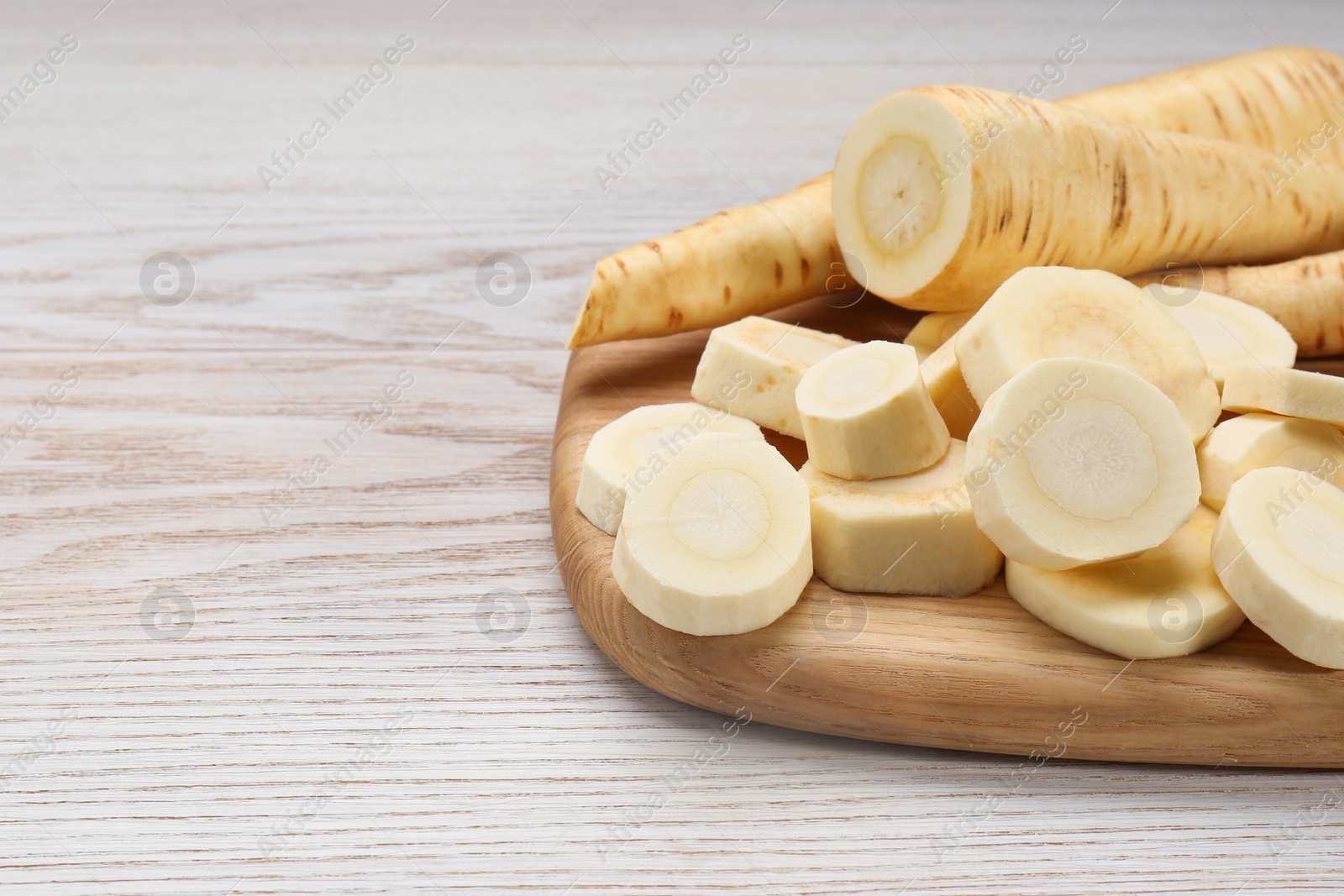 Photo of Whole and cut fresh ripe parsnips on white wooden table, closeup. Space for text