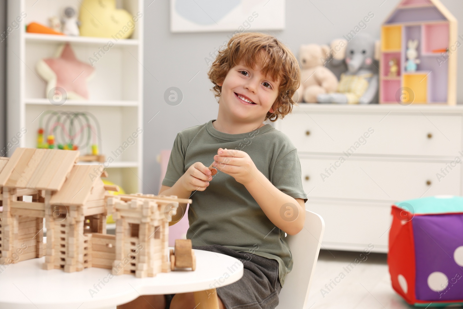 Photo of Little boy playing with wooden entry gate at white table in room. Child's toy