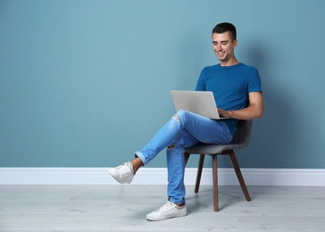 Man in casual clothes with laptop near color wall