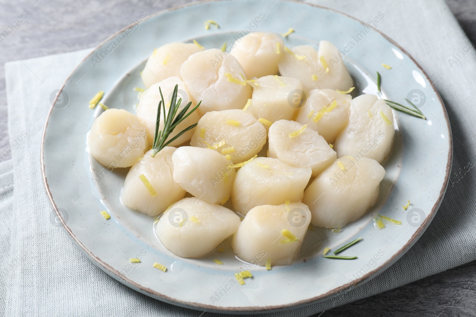 Photo of Raw scallops with lemon zest and rosemary on grey marble table, closeup